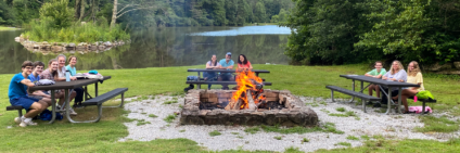 Three families around a campfire next to the lake sitting at three different picnic tables